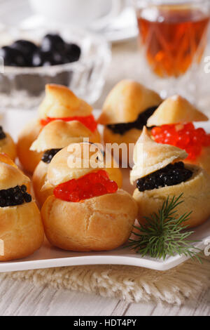 Leckerer Snack: Profiteroles gefüllt mit roten und schwarzen Kaviar auf eine Platte Nahaufnahme. vertikale Stockfoto