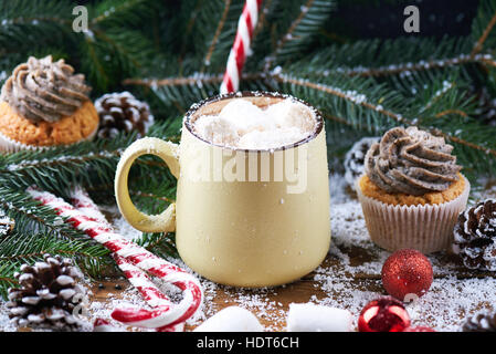 Tasse mit heißer Schokolade und Cup Cake-Schnee-Holztisch Stockfoto
