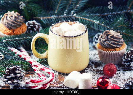 Tasse mit heißer Schokolade und Cup Cake-Schnee-Holztisch Stockfoto