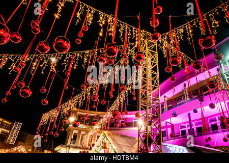 Weihnachtsschmuck-Straße in Velben (Vrba), Österreich. Rote Kugeln hängen, Streichern und gelbe Lichter. Rosa Gebäude im Hintergrund. Stockfoto