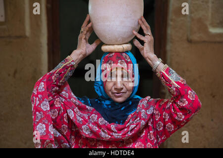 Traditionell gekleidete alte omanischen Frau einen Tontopf auf dem Kopf tragen. Stockfoto