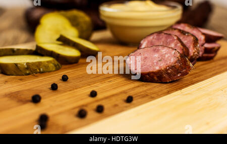 traditionelle hausgemachte geräucherte Schweinswurst mit Gurke auf Holztisch Stockfoto