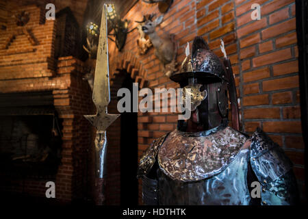 Mittelalterlicher Krieger Soldat Metall Schutzkleidung tragen. Anzug der Ritter Rüstung stehen im Tample Interieur mit Kamin ausgestopfte Tiere auf Ziegelmauer Stockfoto