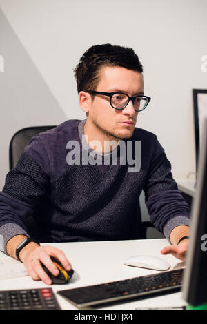 Anstrengenden Arbeitstag. Gut aussehend nachdenklicher junger Mann mit Brille auf Laptop sitzend an seinem Arbeitsplatz Stockfoto