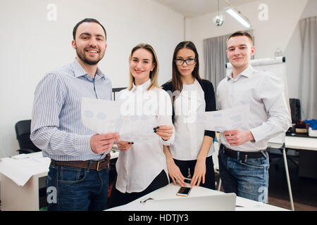 Perfekte Kreativteam. Gruppe von vier fröhliche junge Menschen Blick in die Kamera Lächeln und stützte sich auf den Tisch im Büro Stockfoto
