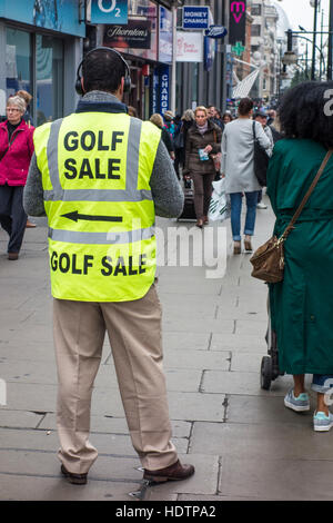 Käufer übergeben Mann trägt Warnschutz-Jacke mit Golf Verkauf Werbeschild. Oxford Street, London Stockfoto