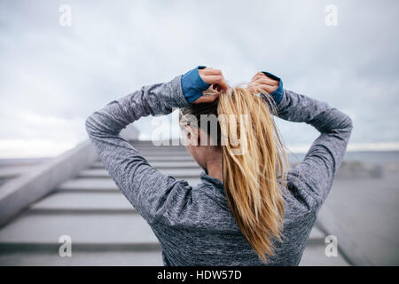 Rückansicht Schuss Fit Sportlerin binden Haare vor ihrem Training. Junge Frau, die immer bereit für das Training. Stockfoto