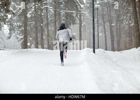 Mann läuft auf Schnee bedeckte Winter-Straße im Wald Stockfoto