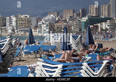 Überfüllten Strand-Szene mit Sonnenliegen und Menschen entspannen oder beim Sport an der Küste mit Wolkenkratzern auf der Rückseite Stockfoto