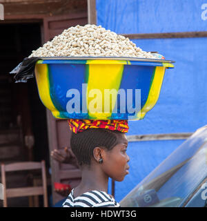 Afrikanische Verkäuferin trägt eine Schale Erdnüsse auf ihrem Kopf Stockfoto