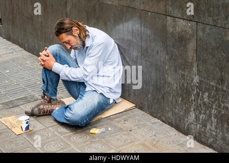 Männlicher Bettler sitzt auf einem Stück Pappe und hat ein Schild auf Pappe, die auf Spanisch, sagt ich bin hungrig, in Barcelona, Spanien. Stockfoto