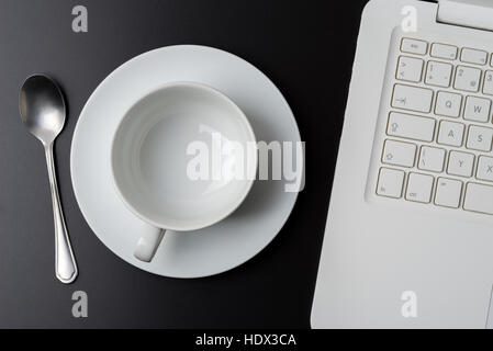 Leere Kaffeetasse neben Laptop auf dunklen natürlichen hölzernen Schreibtisch. Stockfoto