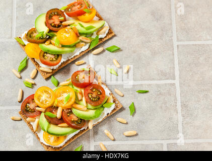 Gesund Roggen Knäckebrot Toast mit Frischkäse, frische Avocado, Cherry Tomaten und Pinienkernen Stockfoto