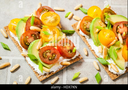 Gesund Roggen Knäckebrot Toast mit Frischkäse, frische Avocado, Cherry Tomaten und Pinienkernen Stockfoto