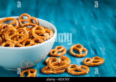 Salzige Snacks Mini Brezeln in Schüssel auf blauen Holztisch Stockfoto