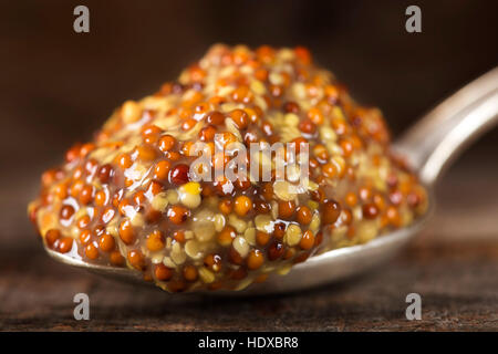 Silberner Löffel gefüllt mit Senfsauce mit Samen und Wein über hölzerne Hintergrund Stockfoto