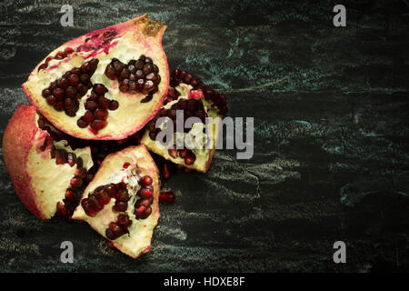 Granatapfel-Frucht halbieren auf einem dunklen Hintergrund mit roten Samen. Gesunde Ernährung, Diät oder Koch-Konzept. Veganes Essen. Rohe Stockfoto