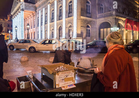 Eine Frau kauft heißen Maroni aus einem Straßenhändler in Praça Dom Pedro lV, Lissabon Portugal Stockfoto