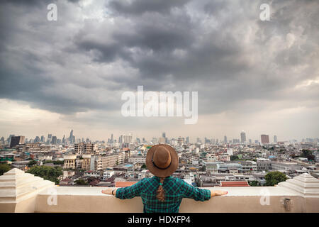 Tourist-Frau in Hut und grün kariertes Hemd Blick auf Bangkok City Panorama mit Wolkenkratzern des Geschäftsviertels von Golden Mountain Wat Saket vie Stockfoto