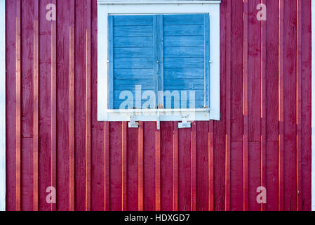 Geschlossenen blauen Fenster Rollladen mit weißem Rahmen auf roten Holzgebäude. Stockfoto