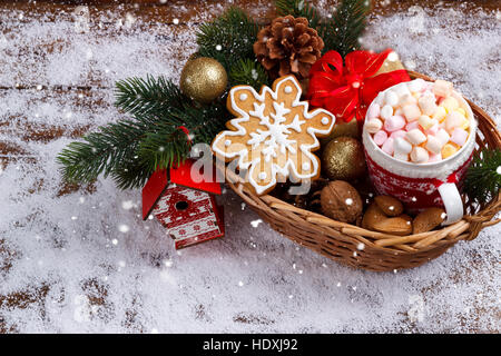 heiße Schokolade mit geschmolzenen Marshmallows, Ingwer Brot Keksen, Nüssen in Weidenkorb auf Schnee. Textfreiraum Stockfoto