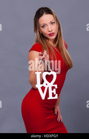 Valentines Day. Frau mit roten Kleid grau hinterlegte Symbol Zeichen Liebe festhalten Stockfoto