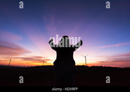 Silhouette touristischen Frau hob die Hand bis zum Sonnenuntergang auf die Turbine am Stausee bei schwachem Licht Stockfoto