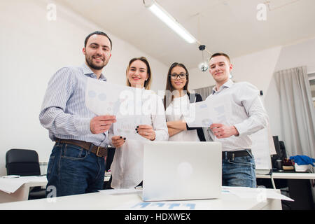 Perfekte Kreativteam. Gruppe von vier fröhliche junge Menschen Blick in die Kamera Lächeln und stützte sich auf den Tisch im Büro Stockfoto