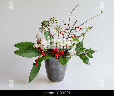 Winter Beeren, Laub & Blumen in einer Vase Keramik "Studio". Zwergmispel,, Garrya, Blumen, Efeu, Viburnum und Kirschbaum. Stockfoto