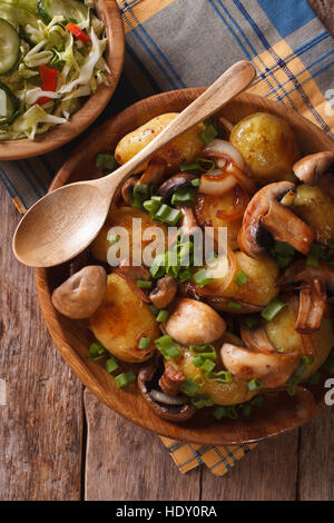 Bratkartoffeln mit Champignons hautnah in eine Schüssel geben und frischen Salat im rustikalen Stil. vertikale Ansicht oben Stockfoto