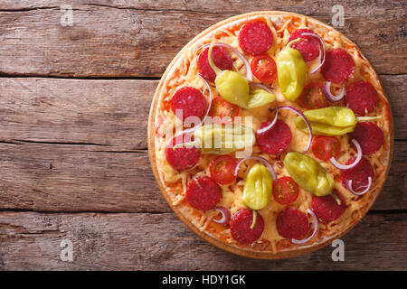 Pizza mit Salami, Peperoni, Paprika, Tomaten und Zwiebeln in einer Tabelle Nahaufnahme vertikale Ansicht von oben, rustikal Stockfoto