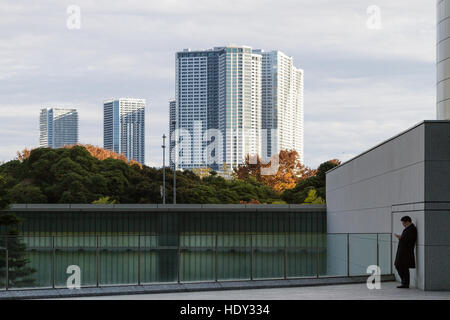 Ein Salaryman lehnt sich an eine Wand und benutzt ein Smartphone, Shiodome, Shimbashi, Tokio, Japan. Stockfoto