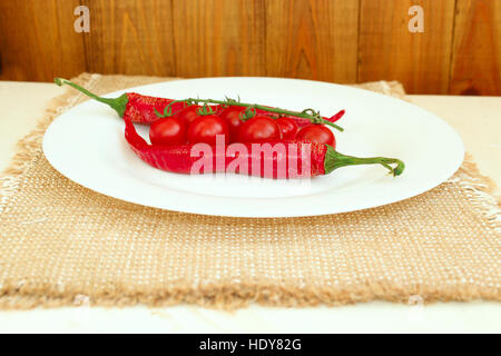 Zweig der rote Kirschtomaten und zwei Pods von Chilischoten auf dem Teller Stockfoto