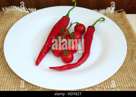 zwei Pods der Chili Peppers und Zweig der rote Cherry-Tomaten auf dem Teller Stockfoto