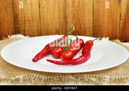 Hülsen von Chili Peppers und Zweig der rote Cherry-Tomaten auf dem Teller Stockfoto