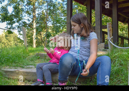 Zwei Schwestern sitzen und spielen zusammen im japanischen Garten auf den schönen sonnigen Tag Stockfoto