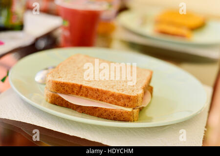 Nahaufnahme eines Sandwich gefüllt mit Schinken und Käse in eine keramische Platte, auf einen Tisch für Frühstück oder Brunch, mit einem Glas mit einem roten Smoothie in der b Stockfoto