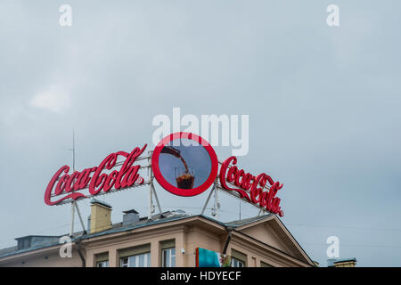 BELARUS, MINSK - 17. August 2016: Neon-Schilder mit einigen berühmten Marke - COCA COLA. Anzeige im Centrum der Stadt stehen oben aufbauend auf Dach gegen blauen Himmel Stockfoto