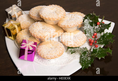 Traditionelle Mince Pies mit einer Prise Puderzucker auf einem weißen Teller mit einem Zweig der Stechpalme Stockfoto