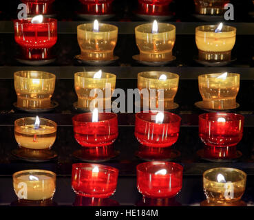 Reihe von Votiv Kerzen in kleinen farbigen Glas Gläser Rot und Gelb platziert und auf Holzregale in einer Kirche Stockfoto