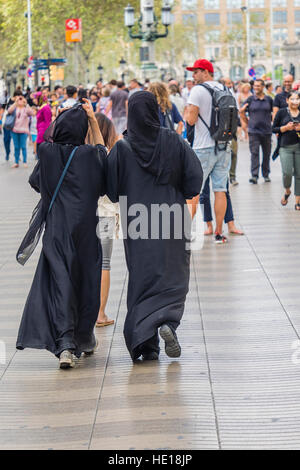 Zwei muslimische Frauen tragen schwarze farbige Burkas gehen gemeinsam entlang der berühmten walking street La Rambla in Barcelona, Spanien. Stockfoto