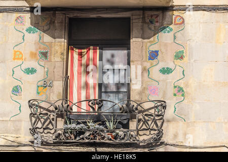 Ein Balkon in Barcelona, Spanien mit der katalanischen Flagge angezeigt, kunstvolle Schmiedearbeiten und polychrome Blumen gemalt an der Fassade des Gebäudes. Stockfoto