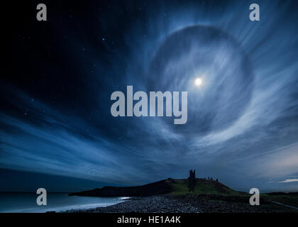 Ein 22° lunar Heiligenschein über Dunstanburgh Castle in Northumberland Küste im Vereinigten Königreich Stockfoto