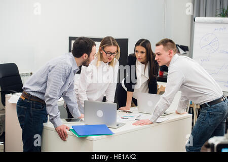 Junge Geschäftsleute sitzen im Büro während der treffen und diskutieren mit Papierkram mit Notebooks Stockfoto