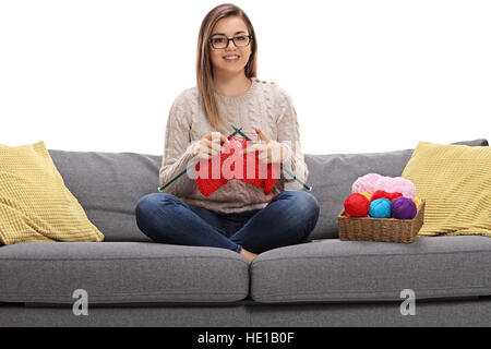 Fröhliche Mädchen auf einem Sofa stricken und schaut in die Kamera, die isoliert auf weißem Hintergrund Stockfoto