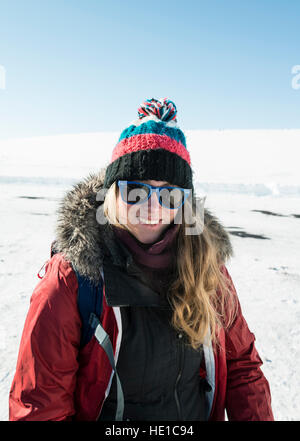 Junge Frau trägt Winterjacke und Wollmütze, lächelnd, Schneelandschaft, Island Stockfoto