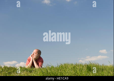 Junger Mann auf einer Wiese liegend stützen den Kopf in seinen Händen Stockfoto
