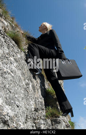 Geschäftsfrau aufsteigend eine steile Felswand klettern Stockfoto