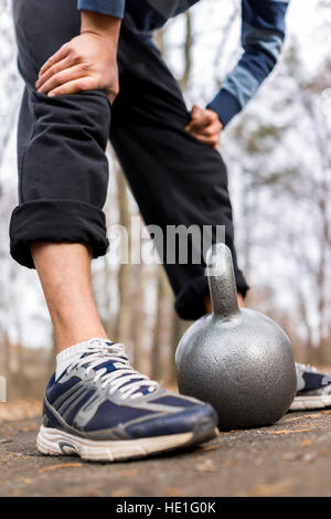 Nahaufnahme der Kettlebell am Boden durch Mannes Turnschuhe außerhalb Stockfoto