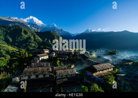 Blick auf das historische Dorf mit den Bergen Annapurna Süd (links), Himchuli (Mitte) und Machapuchare (rechts) in der Ferne bei Sonnenaufgang, Smok ist Stockfoto